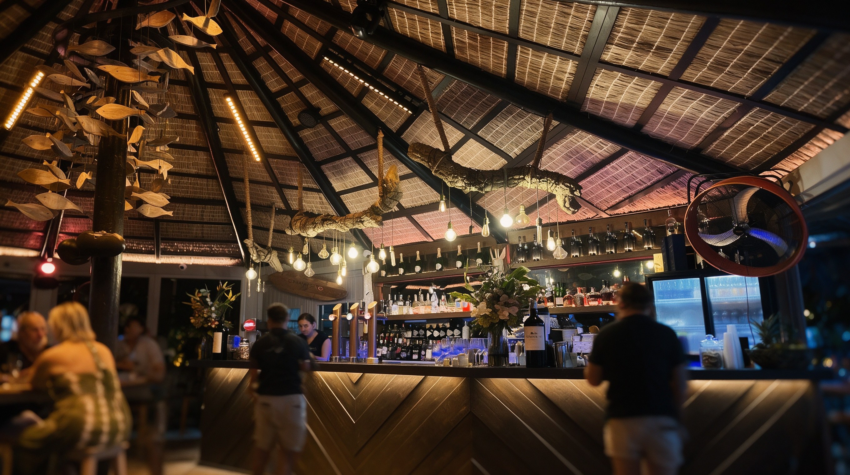 Barra de restaurante con techo de caña tropical, luces cálidas y botellas al fondo en la noche